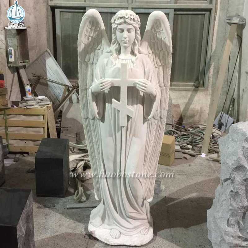 天使の彫刻が立っている白い大理石の十字架
